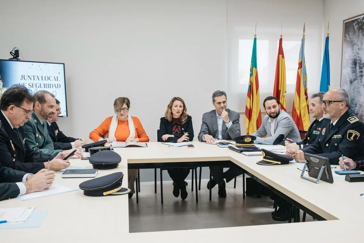 Reunión de una junta local de seguridad con autoridades civiles y mandos policiales sentados alrededor de una mesa en forma de U con banderas oficiales al fondo