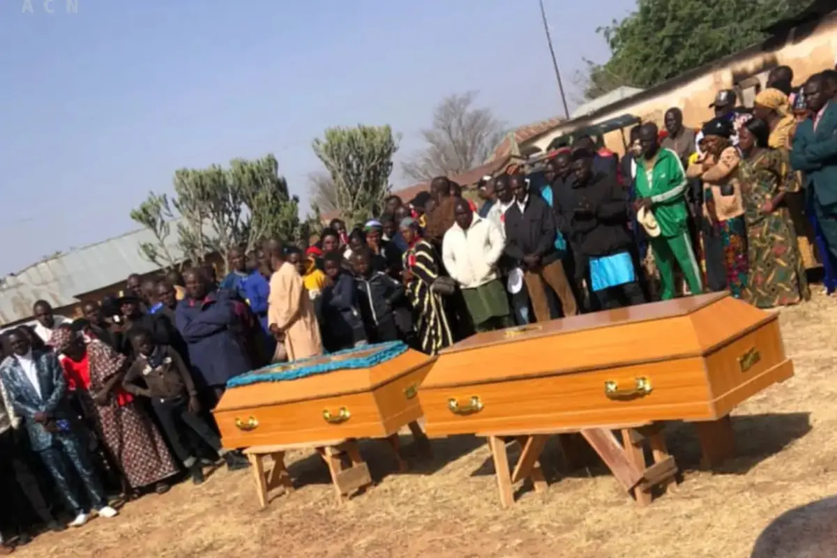 Un grupo de personas reunidas al aire libre alrededor de dos ataúdes de madera durante un funeral