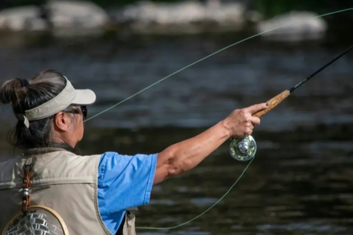 Persona pescando con caña en un río usando chaleco y visera Persona pescando con caña en un río usando chaleco y visera
