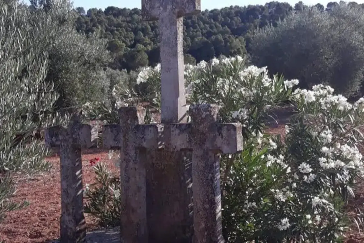 Cruz de piedra envejecida rodeada de vegetación y flores blancas en un entorno natural