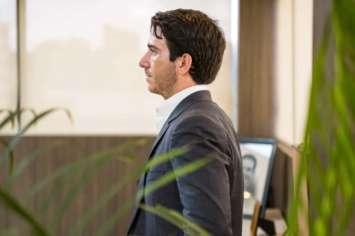 Hombre de perfil con traje gris en una oficina moderna con plantas en primer plano