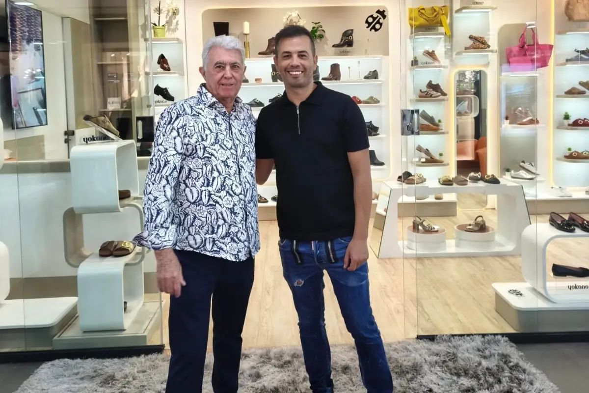Dos hombres posan sonrientes en el interior de una zapatería moderna con estanterías llenas de calzado al fondo