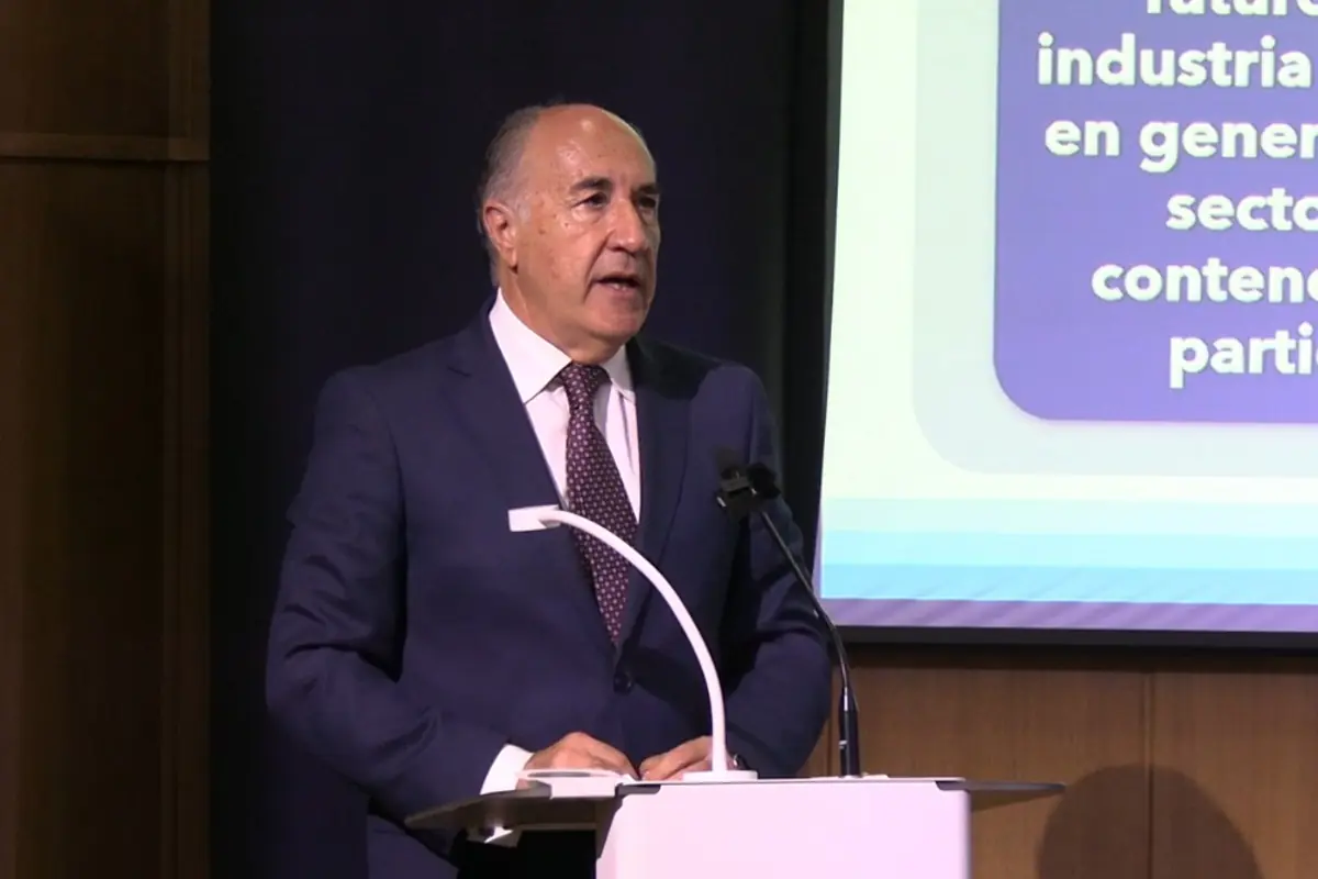 Hombre de traje hablando en un podio frente a una pantalla con texto durante una presentación o conferencia