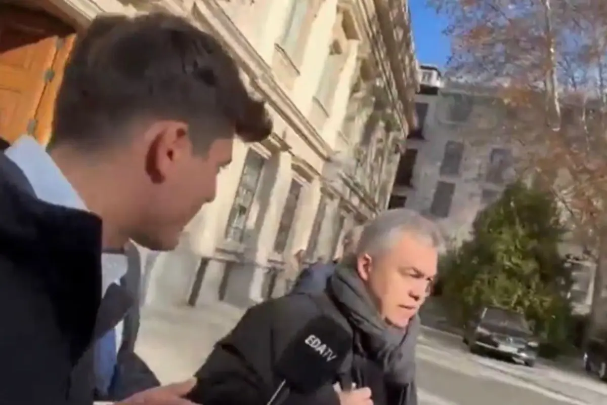 Reportero con micrófono de EDATV intenta entrevistar a un hombre de cabello canoso que camina por la calle junto a un edificio histórico