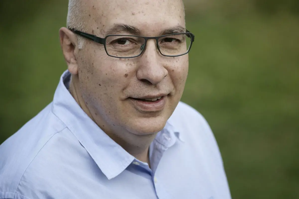 Retrato de un hombre calvo con gafas y camisa azul claro mirando a la cámara con fondo verde desenfocado