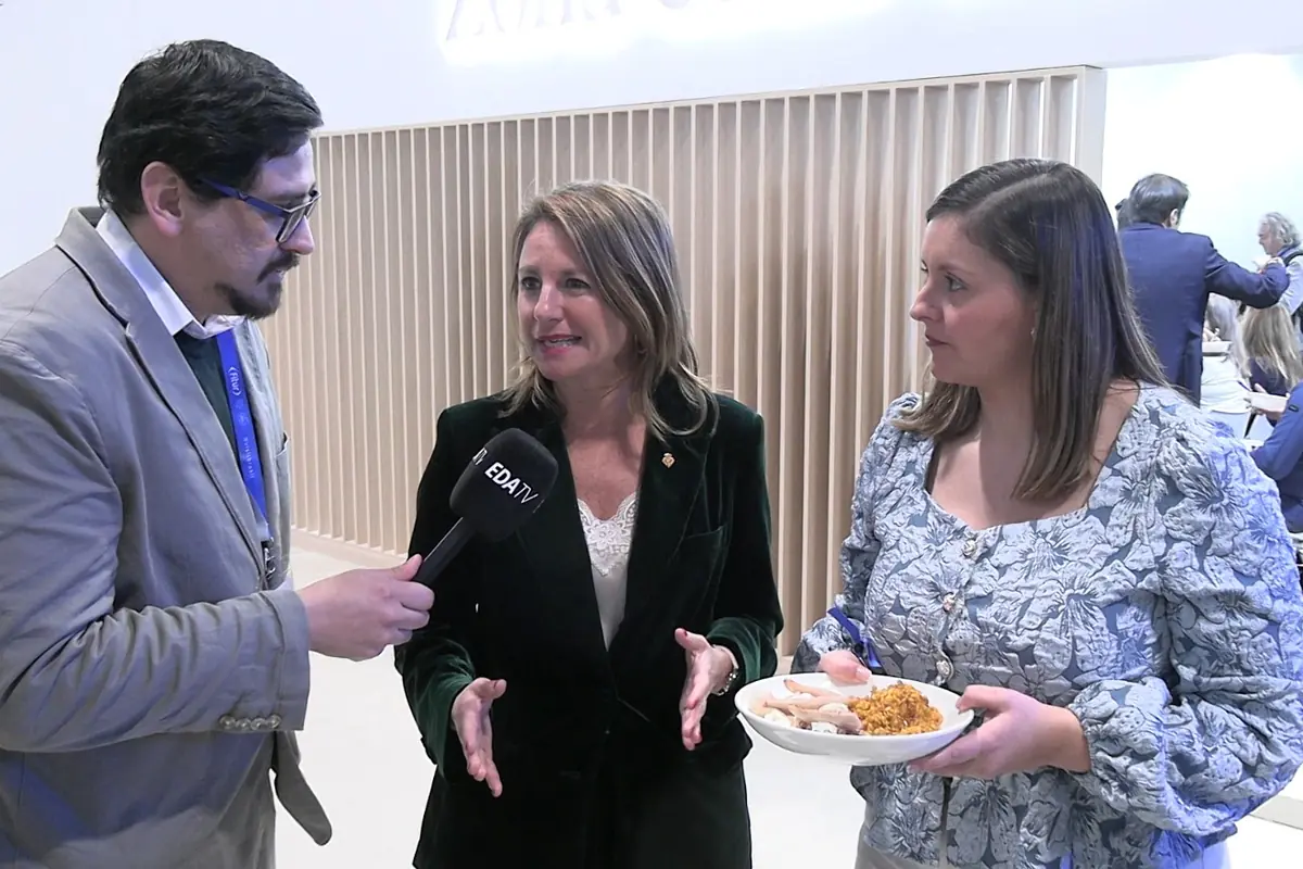 Periodista entrevistando a una mujer mientras otra sostiene un plato de comida en un evento o feria profesional