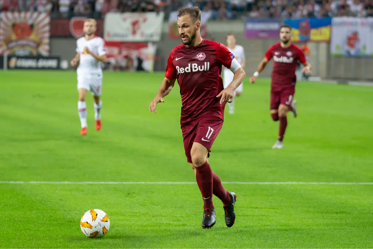 Futbolista del Red Bull Salzburg con uniforme granate corre hacia el balón durante un partido en un estadio lleno