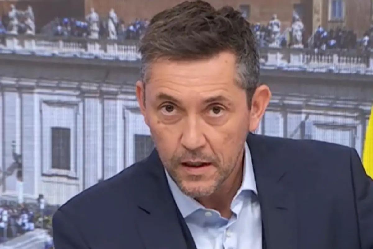 Hombre de mediana edad con traje azul hablando frente a un fondo urbano con edificio histórico desenfocado Hombre de mediana edad con traje azul hablando frente a un fondo urbano con edificio histórico desenfocado