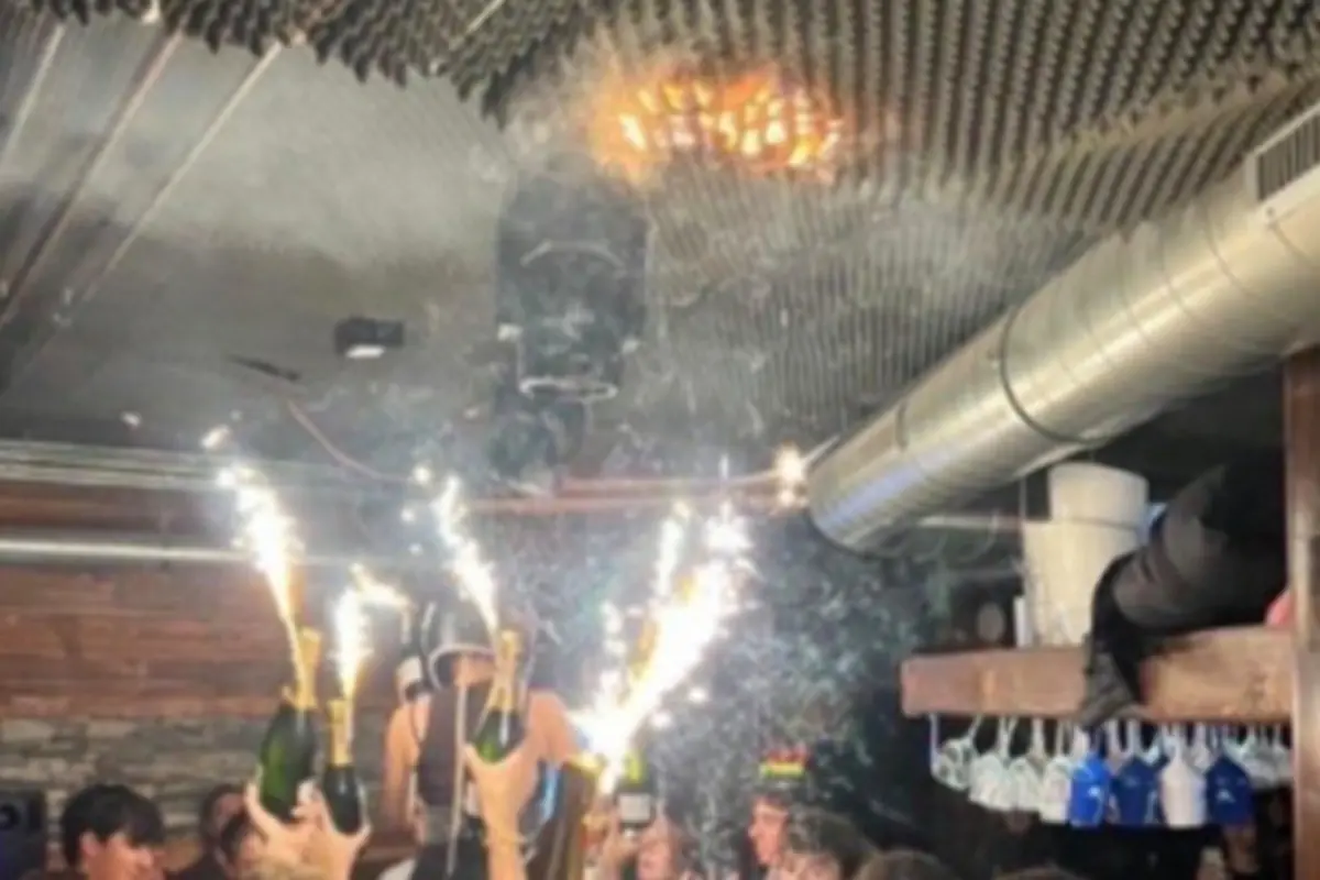Personas celebrando en un bar cerrado levantan botellas de champán con bengalas encendidas mientras el techo comienza a incendiarse por las chispas Personas celebrando en un bar cerrado levantan botellas de champán con bengalas encendidas mientras el techo comienza a incendiarse por las chispas