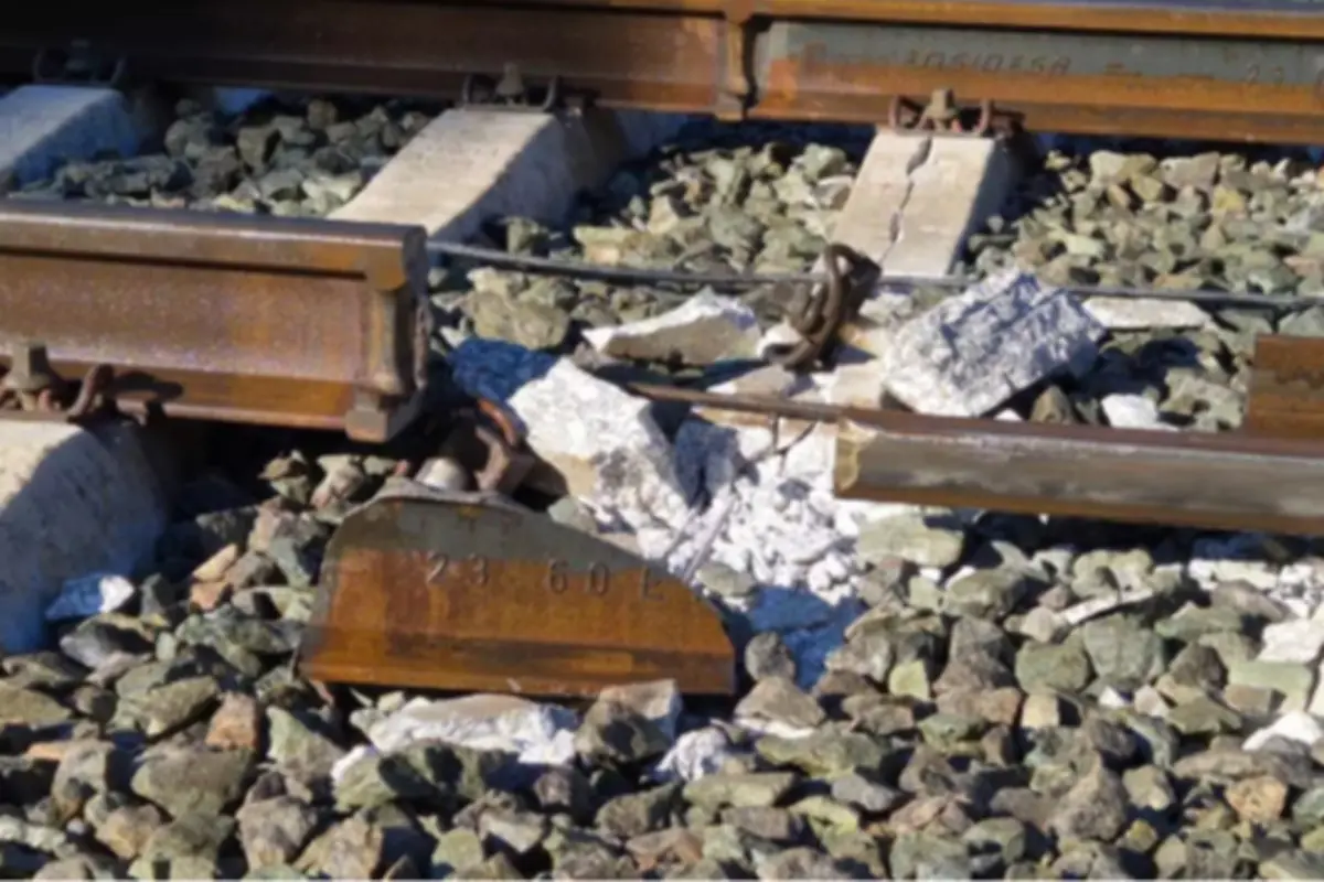 Vía férrea rota con un tramo de riel oxidado desprendido y traviesas de hormigón fracturadas entre piedras de balasto Vía férrea rota con un tramo de riel oxidado desprendido y traviesas de hormigón fracturadas entre piedras de balasto