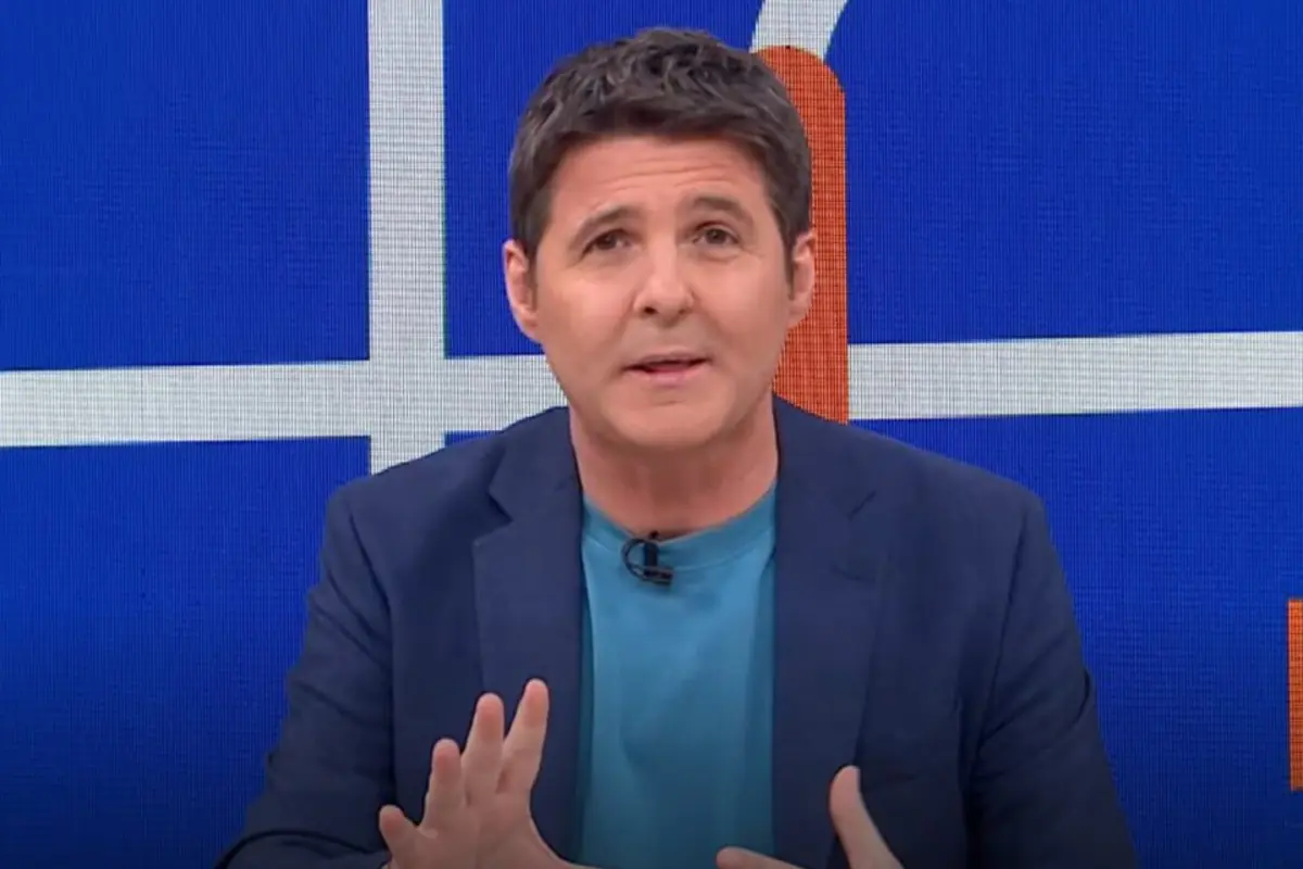 Presentador de televisión de mediana edad hablando a cámara con chaqueta azul y camiseta turquesa sobre un fondo azul con líneas blancas y naranjas Presentador de televisión de mediana edad hablando a cámara con chaqueta azul y camiseta turquesa sobre un fondo azul con líneas blancas y naranjas