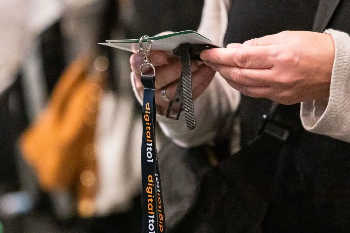 Persona sosteniendo una acreditación con lanyard azul de evento tecnológico en un entorno concurrido