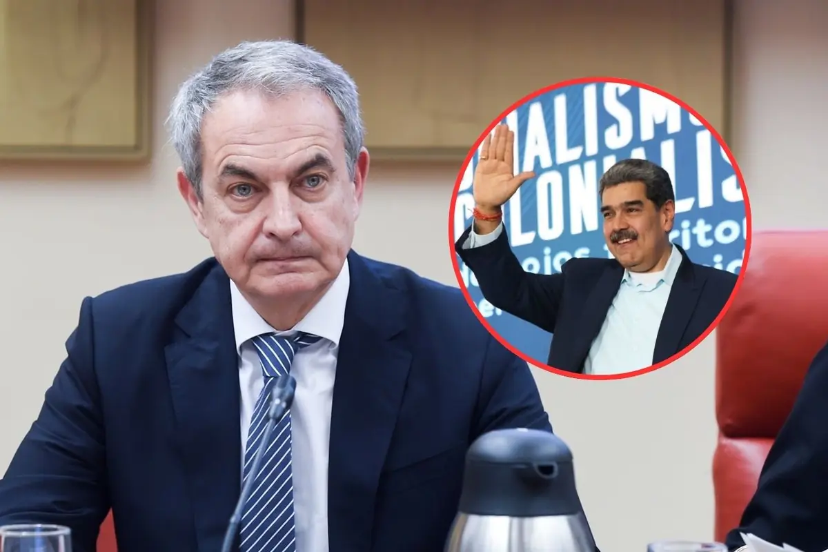 Hombre de traje serio en una reunión con un micrófono y una jarra metálica sobre la mesa y un recuadro circular que muestra a otro hombre saludando con la mano levantada frente a un fondo azul con texto