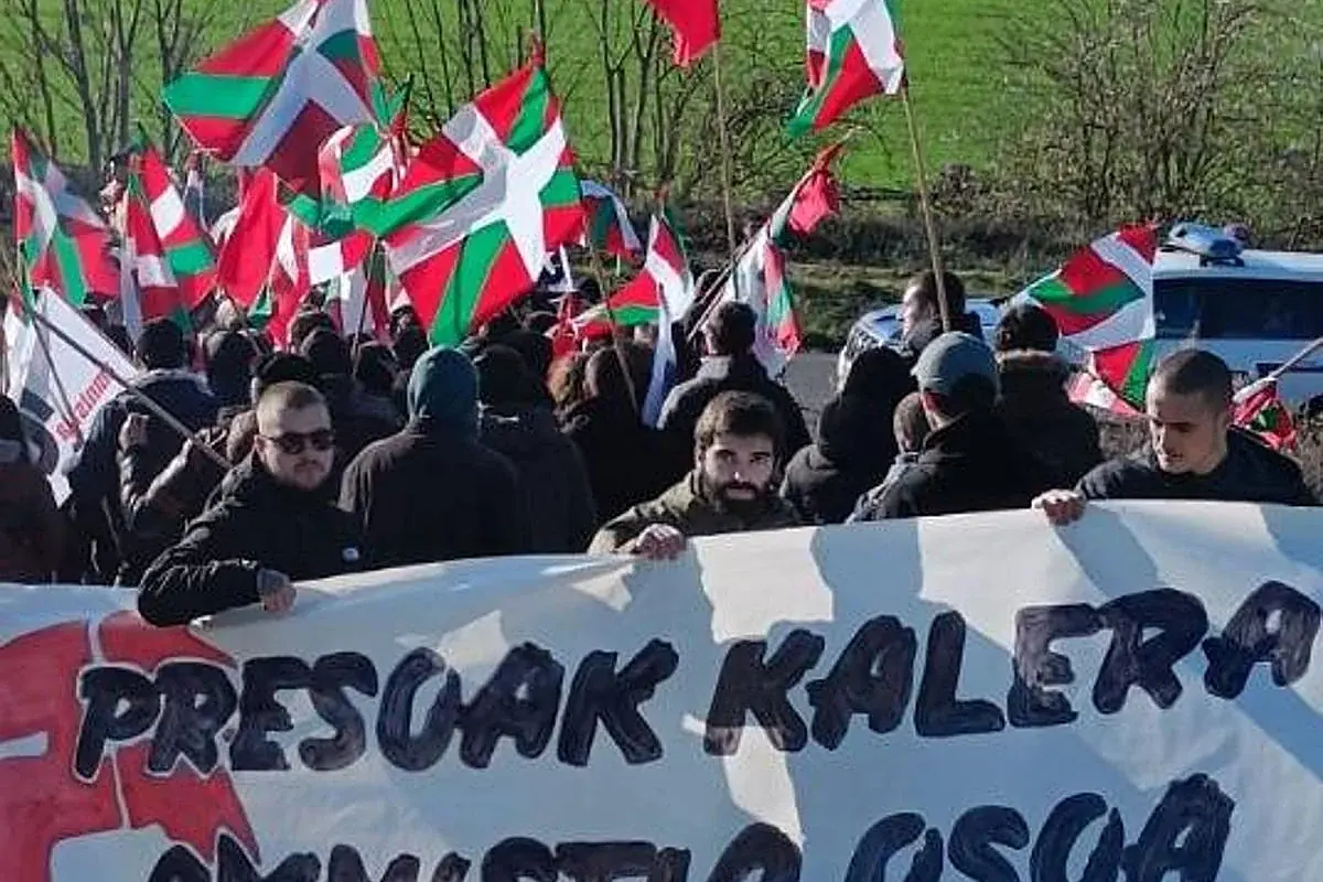 Manifestación con numerosas personas portando banderas vascas y una pancarta grande en euskera en primer plano Manifestación con numerosas personas portando banderas vascas y una pancarta grande en euskera en primer plano
