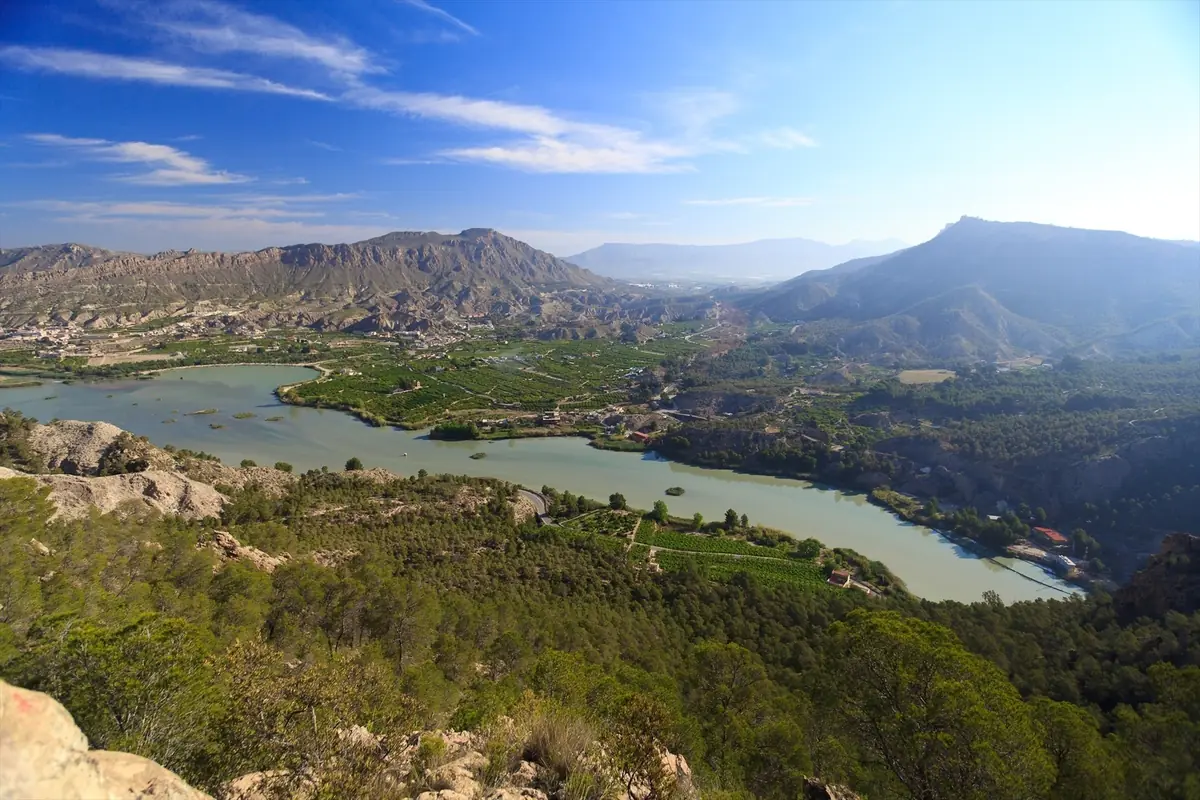 Panorámica de un valle verde con un río ancho serpenteando entre montañas rocosas bajo un cielo azul despejado