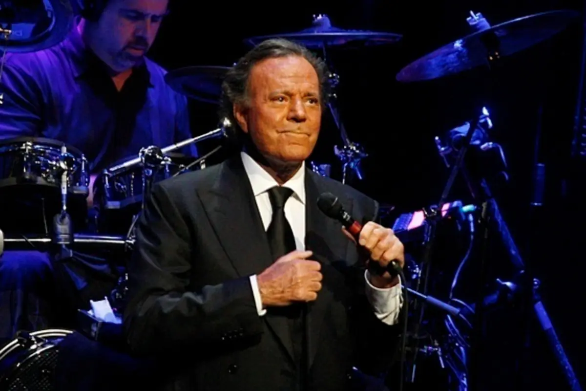 Cantante de traje oscuro sosteniendo un micrófono mientras actúa en un escenario con batería al fondo