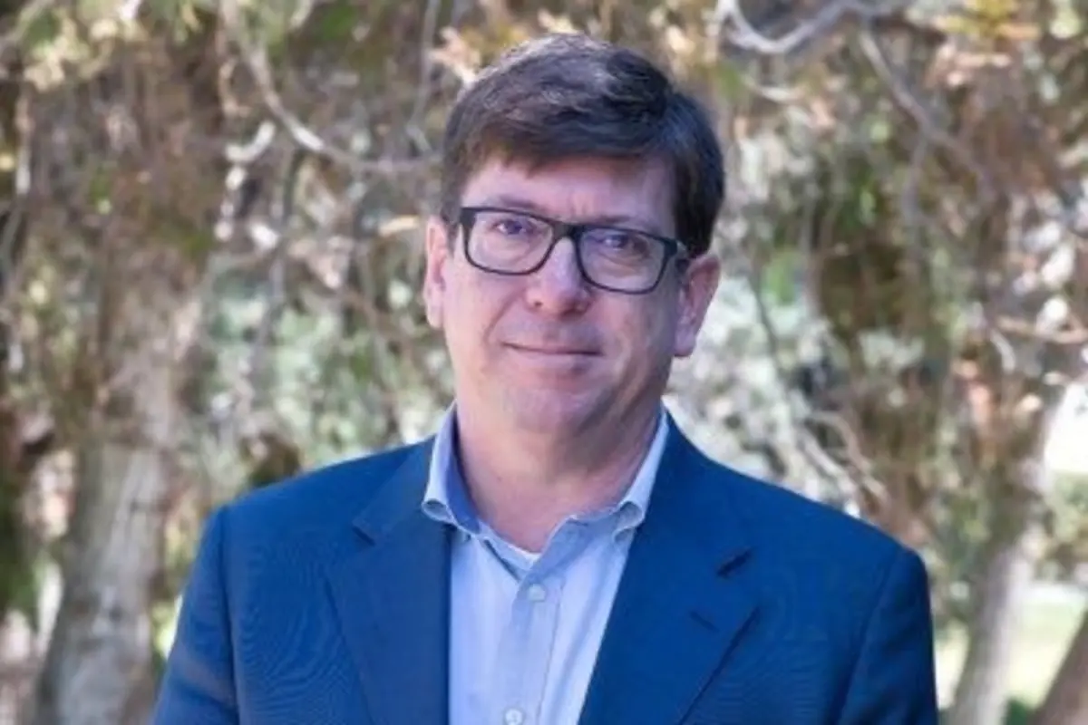 Hombre de mediana edad con gafas y traje azul posando al aire libre frente a árboles desenfocados Hombre de mediana edad con gafas y traje azul posando al aire libre frente a árboles desenfocados