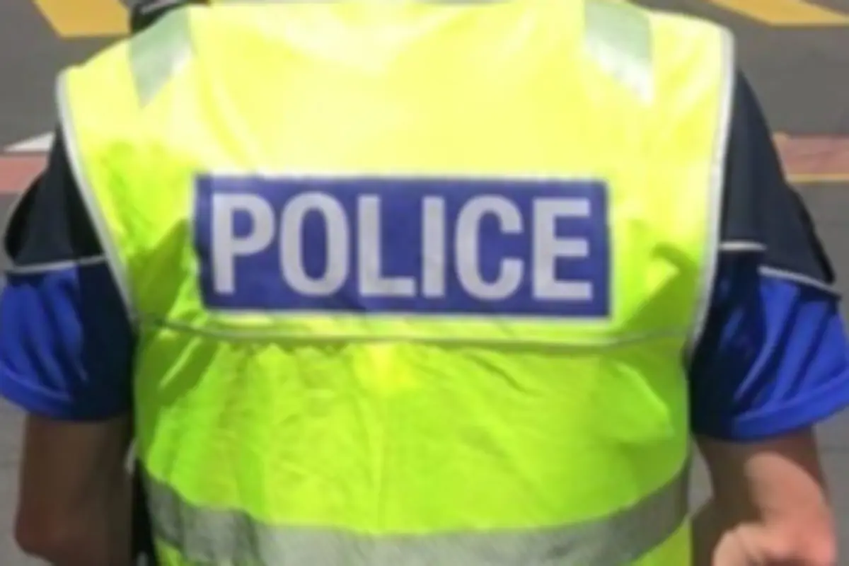 Agente de policía de espaldas con chaleco reflectante amarillo que lleva la palabra POLICE en grande