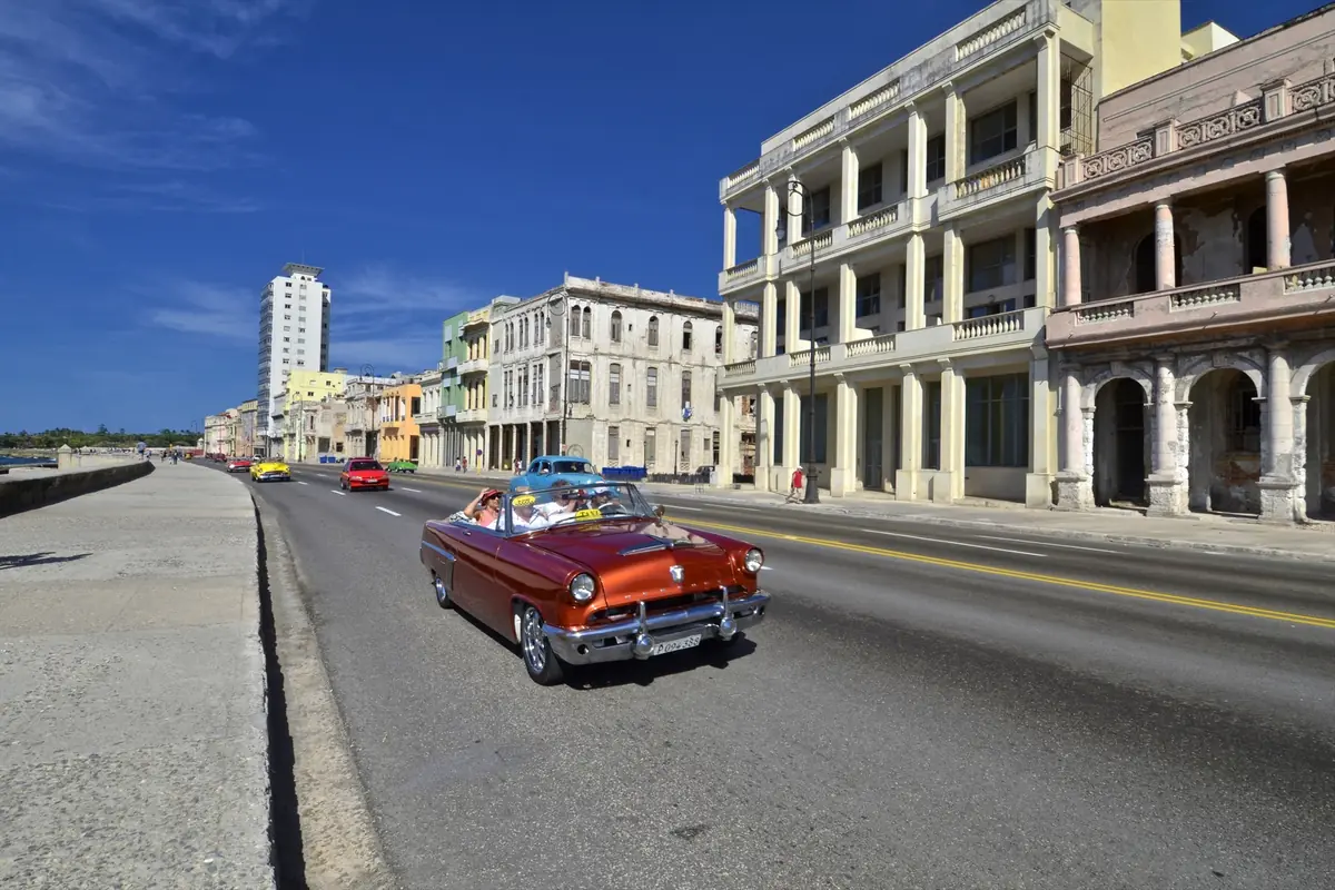 Auto clásico rojo descapotable circulando por el Malecón de La Habana junto a edificios antiguos y cielo azul despejado