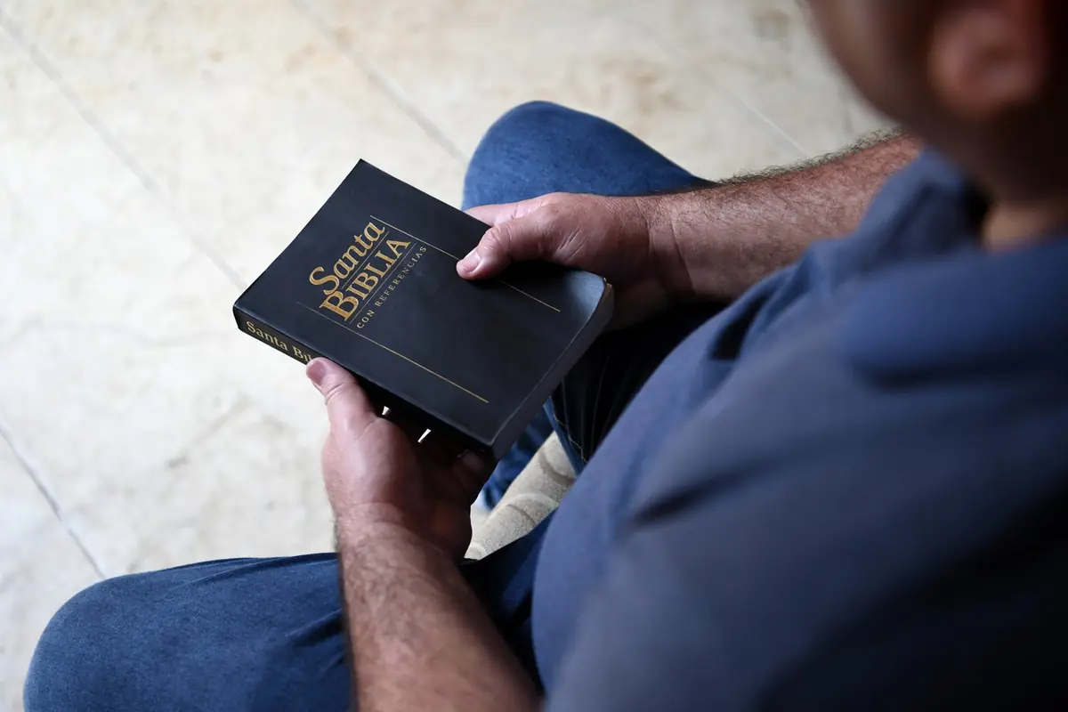Persona sentada sosteniendo una Biblia en español con tapa negra y letras doradas