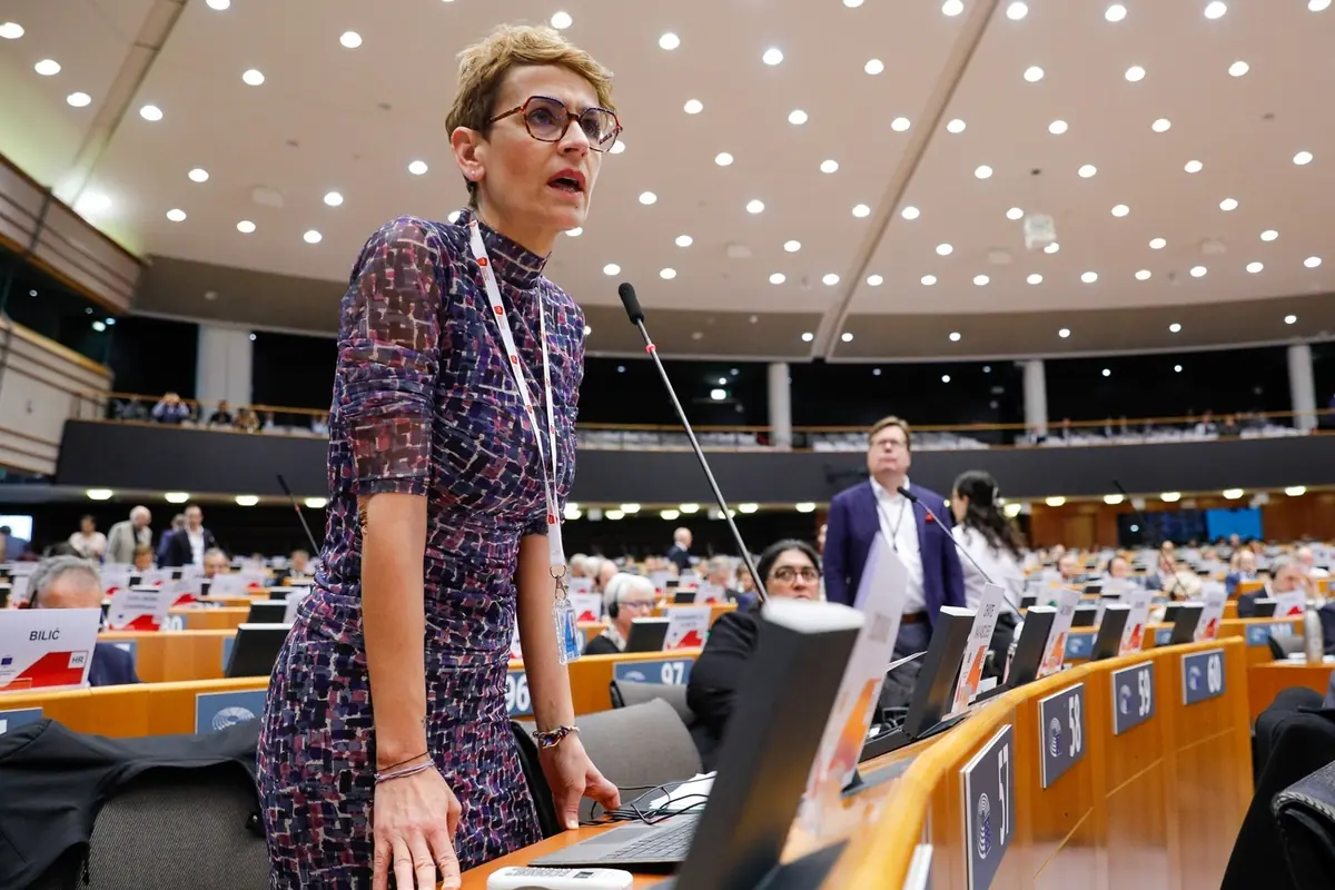 Mujer de pie hablando frente a un micrófono en un gran auditorio lleno de personas y pantallas de ordenador