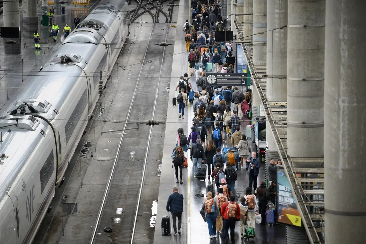 Andén de estación de tren abarrotado de viajeros con maletas junto a un tren de alta velocidad detenido