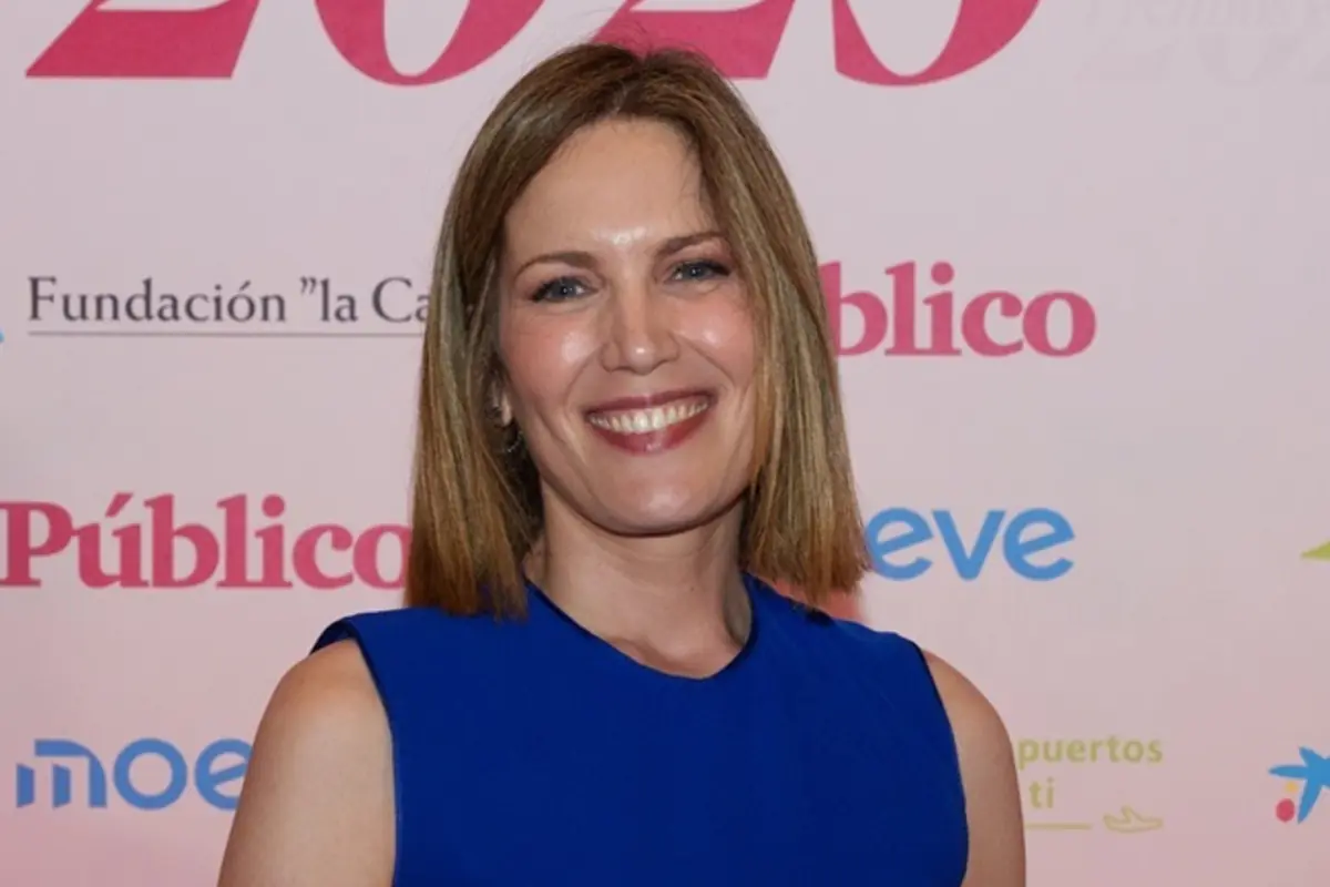 Mujer de pelo castaño liso y media melena sonriendo a cámara con vestido azul en un evento con photocall de fondo Mujer de pelo castaño liso y media melena sonriendo a cámara con vestido azul en un evento con photocall de fondo