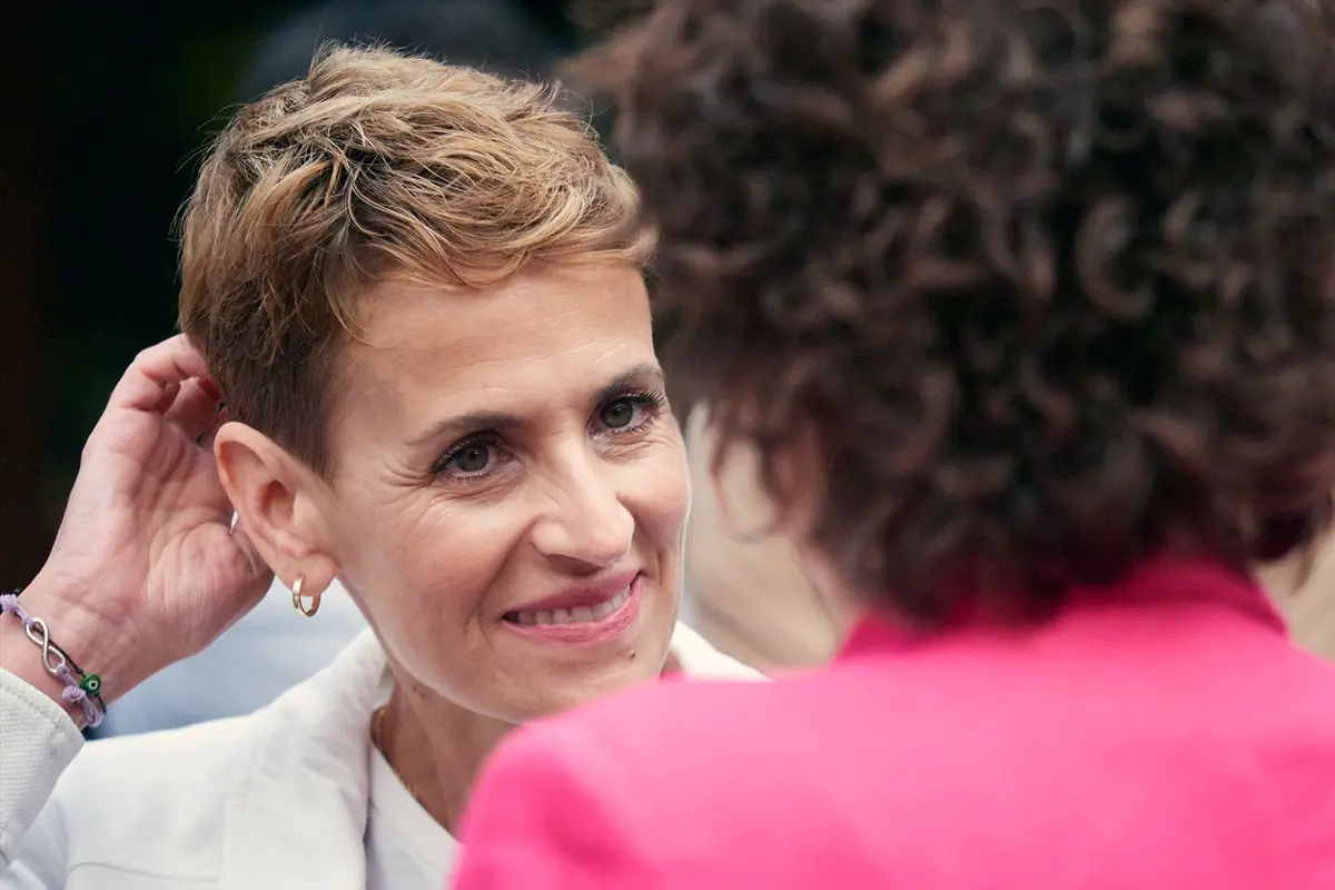 Mujer de pelo corto sonriendo mientras conversa de cerca con otra persona de espaldas con chaqueta rosa