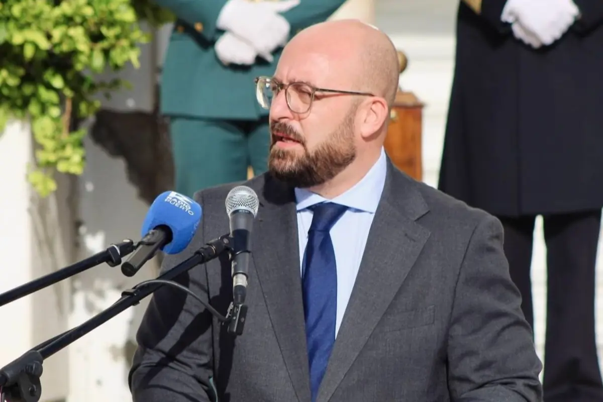 Hombre calvo con barba y gafas hablando frente a varios micrófonos en un acto oficial al aire libre con personal uniformado al fondo Hombre calvo con barba y gafas hablando frente a varios micrófonos en un acto oficial al aire libre con personal uniformado al fondo