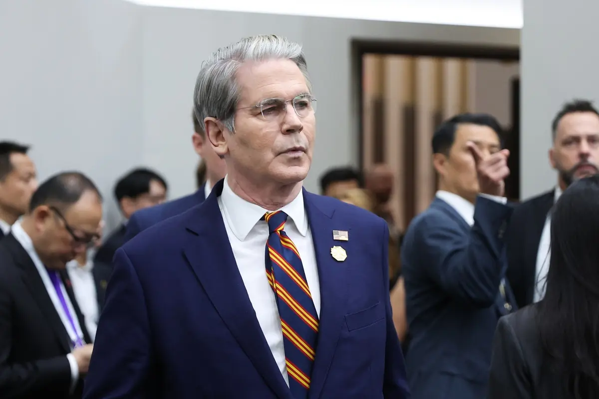 Hombre de cabello canoso con traje azul y corbata a rayas caminando entre otras personas en un evento formal