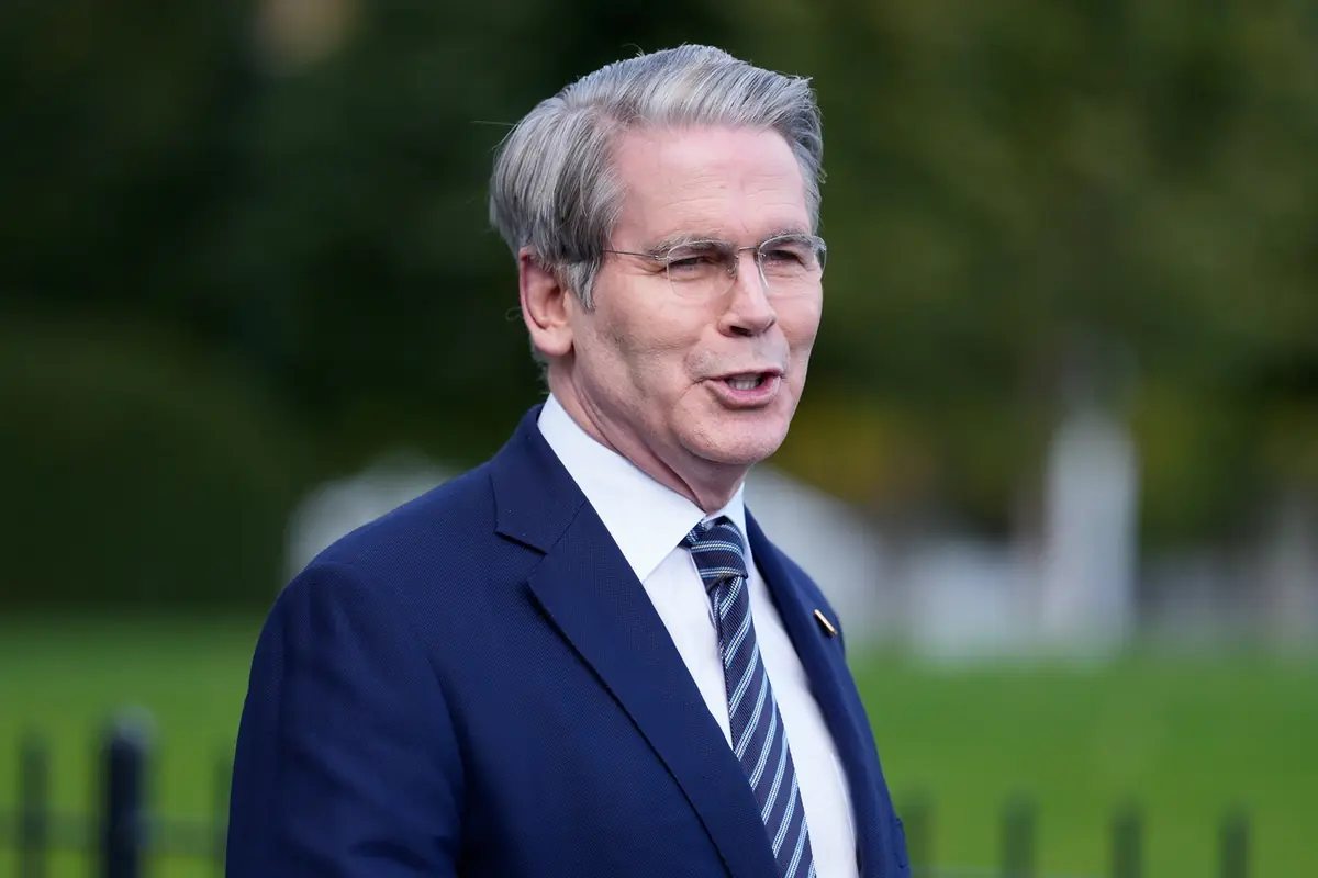Hombre de mediana edad con traje azul y corbata a rayas hablando al aire libre frente a un fondo verde desenfocado
