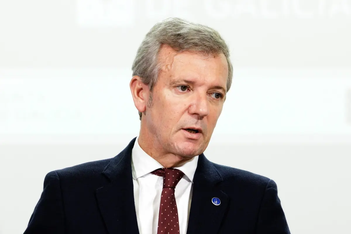 Hombre de mediana edad con traje oscuro y corbata roja hablando en un entorno institucional