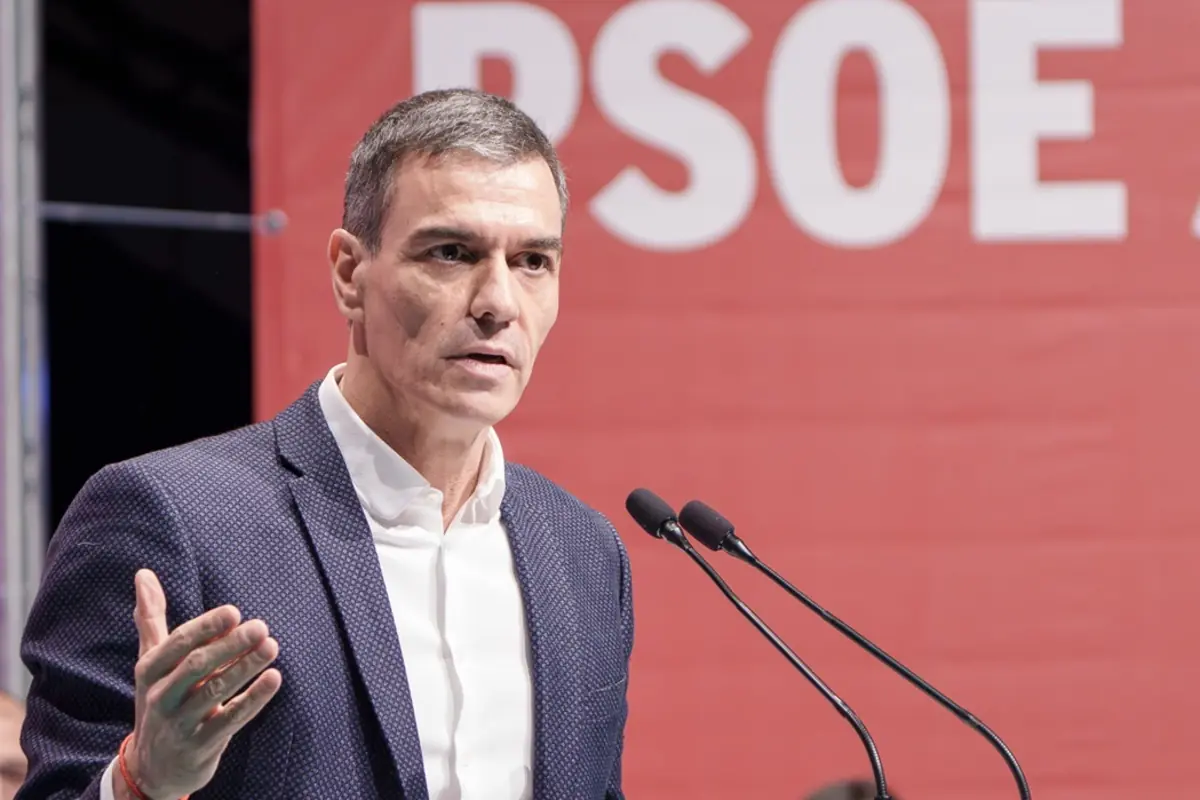 Hombre de mediana edad hablando en un mitin político frente a un micrófono con un gran cartel rojo de fondo donde se leen parcialmente las siglas PSOE Hombre de mediana edad hablando en un mitin político frente a un micrófono con un gran cartel rojo de fondo donde se leen parcialmente las siglas PSOE