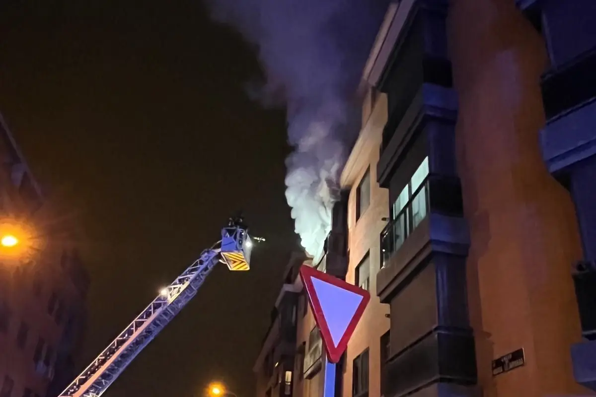 Camión de bomberos con escalera elevadora trabajando de noche en un edificio del que sale una densa columna de humo