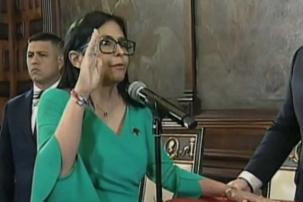 Mujer con gafas y vestido verde levantando la mano derecha y jurando ante un micrófono en un acto oficial Mujer con gafas y vestido verde levantando la mano derecha y jurando ante un micrófono en un acto oficial