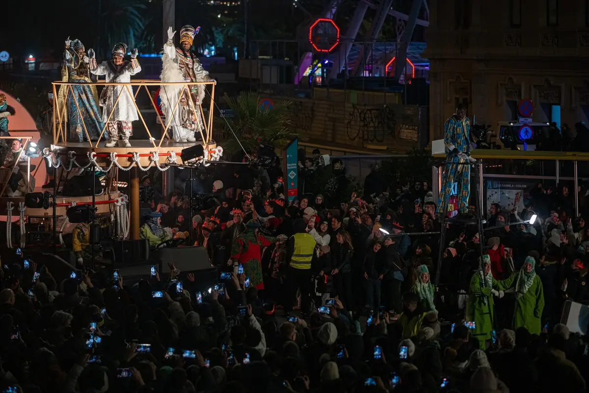 Cabalgata nocturna de los Reyes Magos saludando desde una carroza elevada ante una multitud de personas que los fotografían con sus móviles