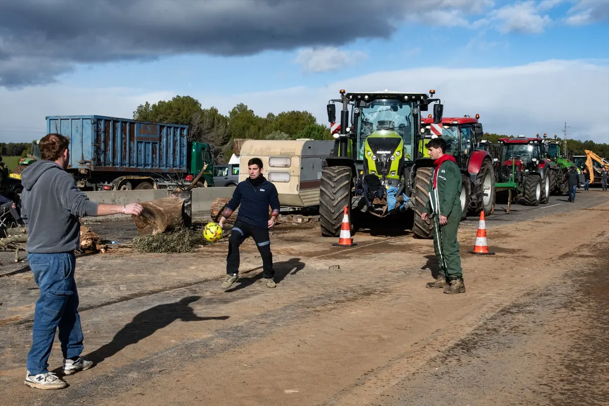 Tres hombres juegan con un balón en una carretera mientras varios tractores y camiones permanecen detenidos al fondo