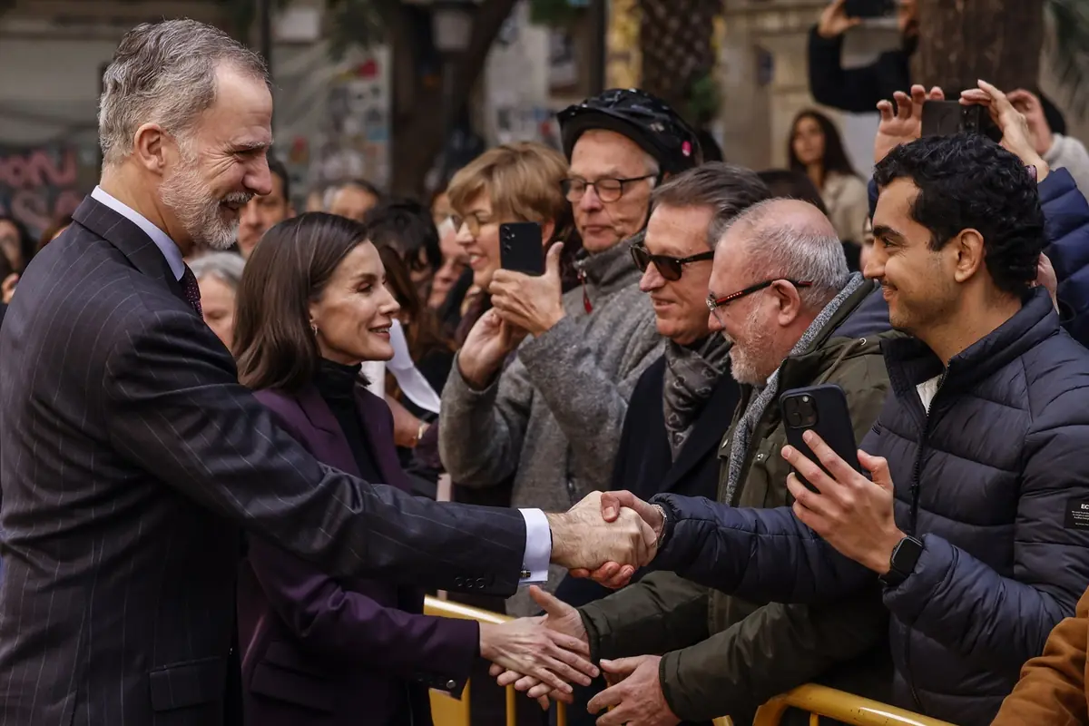 Pareja bien vestida saluda y da la mano a varias personas del público tras una valla mientras algunos asistentes toman fotos con sus móviles Pareja bien vestida saluda y da la mano a varias personas del público tras una valla mientras algunos asistentes toman fotos con sus móviles