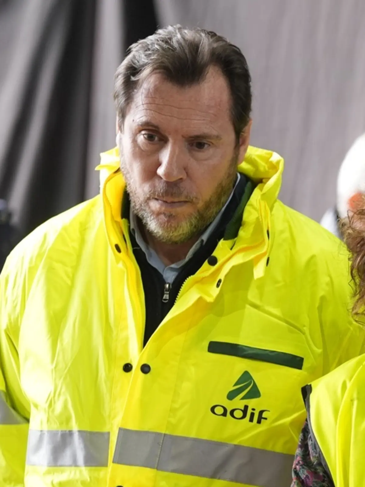 Hombre con chaqueta reflectante amarilla de alta visibilidad con el logotipo de Adif mirando hacia abajo