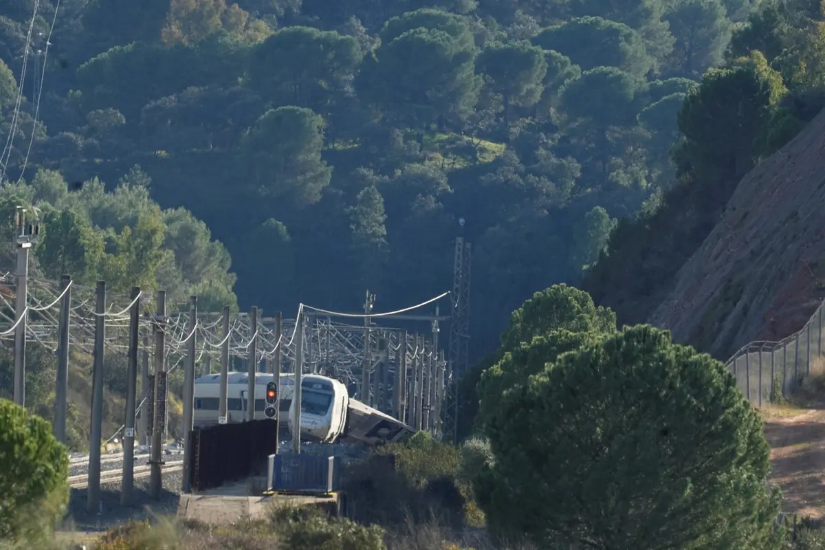 Tren descarrilado en una vía férrea rodeada de postes eléctricos y un denso bosque de pinos en una ladera