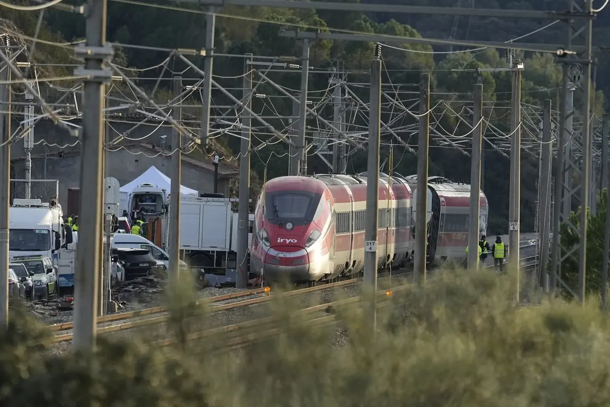Tren de alta velocidad rojo detenido en una vía rodeada de postes eléctricos y vehículos de servicio con varios operarios trabajando en la zona