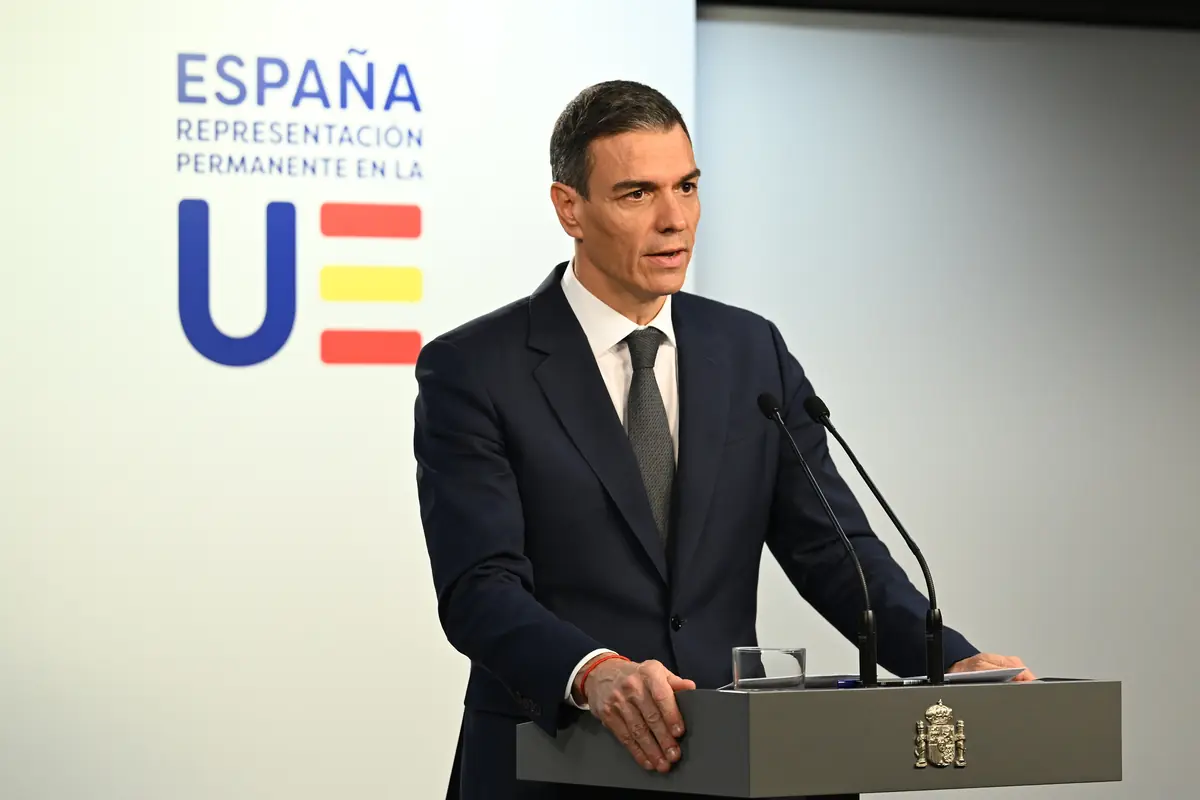 Hombre con traje oscuro dando un discurso en un atril oficial frente a un fondo con el logotipo de la representación permanente de España ante la Unión Europea