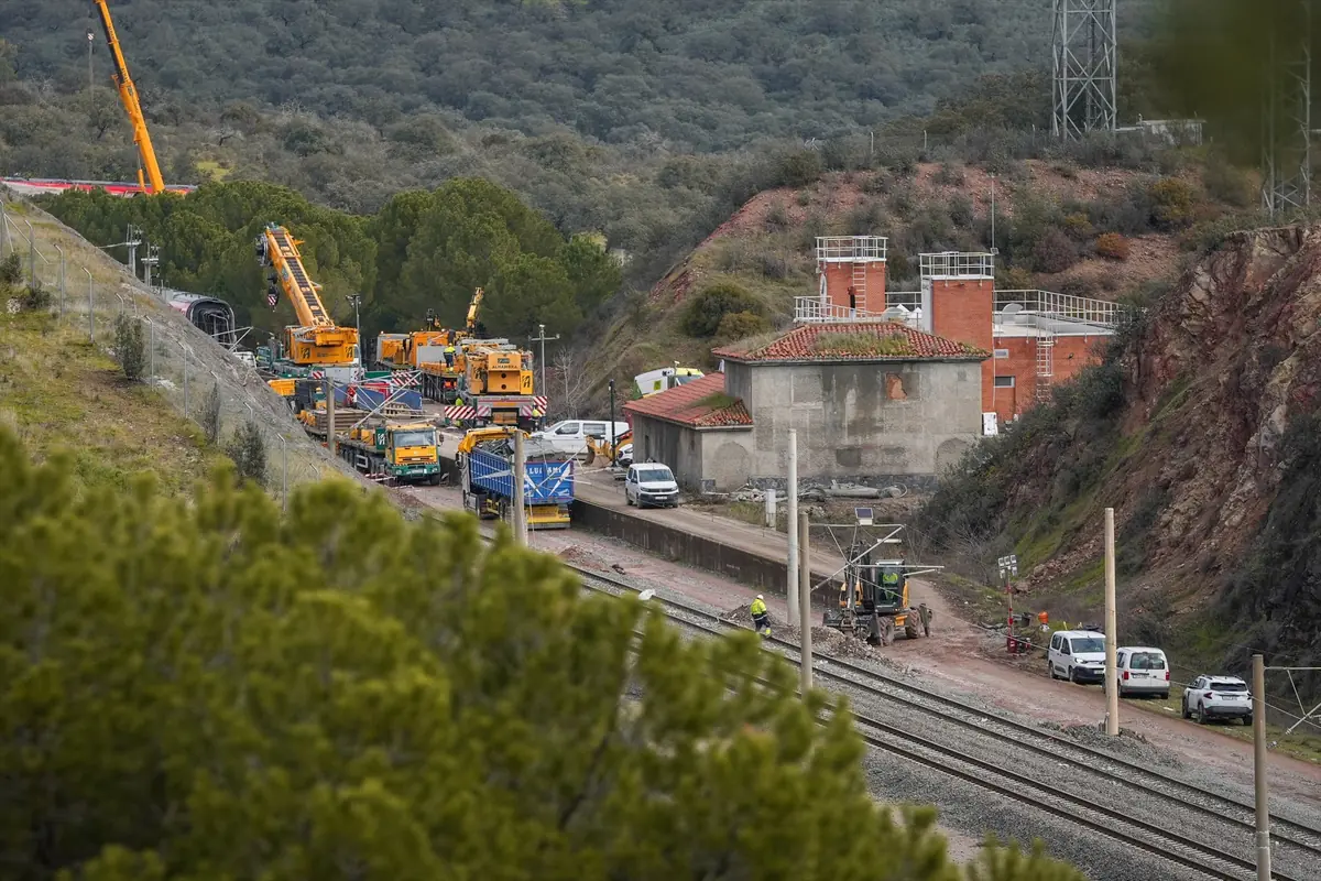 Operarios y maquinaria pesada trabajando en la reparación de una vía de tren en una zona rural con edificios industriales y grúas amarillas Operarios y maquinaria pesada trabajando en la reparación de una vía de tren en una zona rural con edificios industriales y grúas amarillas