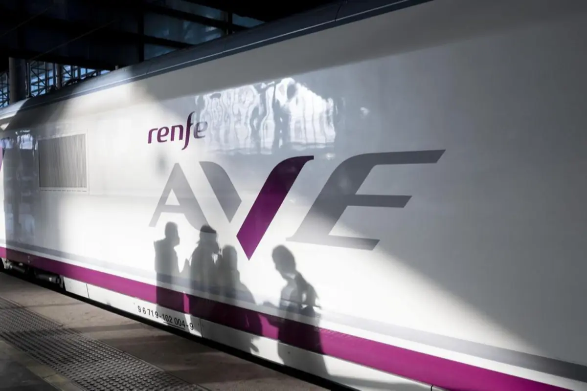 Lateral de un tren de alta velocidad AVE de Renfe en andén con sombras de varios pasajeros proyectadas sobre el vagón