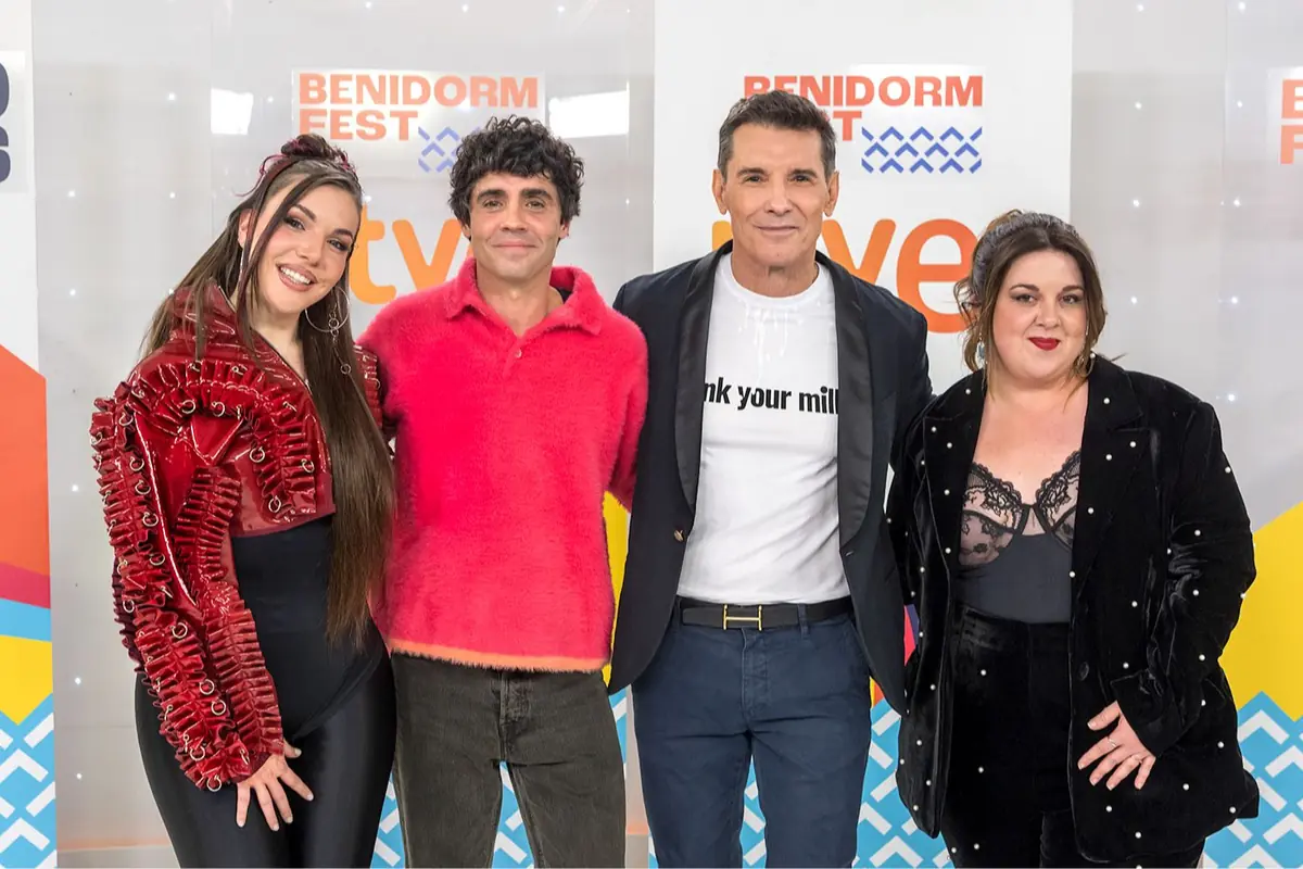 Cuatro personas posan sonrientes frente a un photocall del Benidorm Fest de RTVE con ropa llamativa y de fiesta