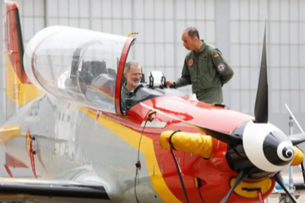 Dos pilotos militares conversan junto a la cabina abierta de un avión de entrenamiento con hélice y fuselaje rojo y amarillo en un hangar Dos pilotos militares conversan junto a la cabina abierta de un avión de entrenamiento con hélice y fuselaje rojo y amarillo en un hangar