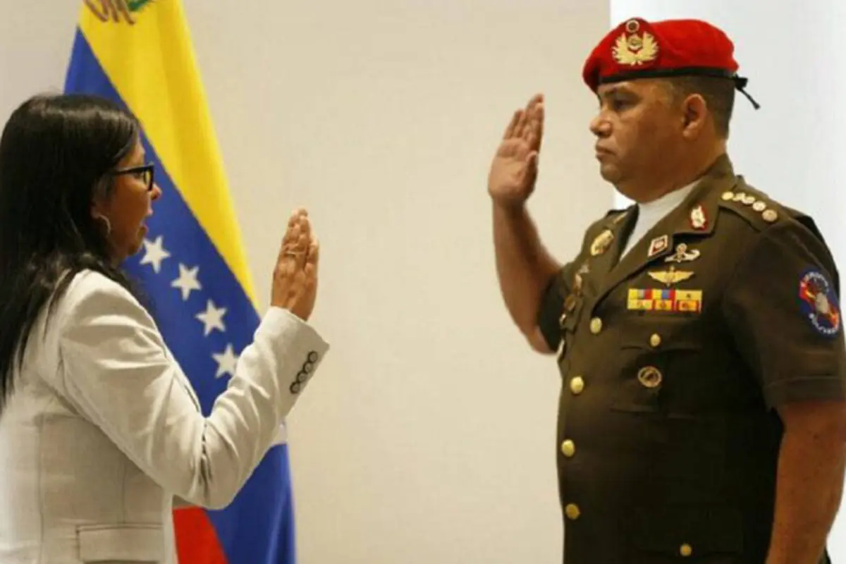 Mujer con saco claro toma juramento a militar con boina roja frente a bandera de Venezuela