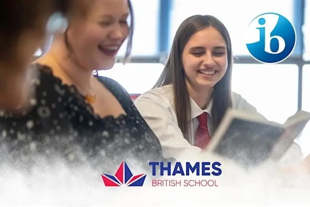 Estudiante y profesora sonríen mientras leen en un aula con el logotipo del Bachillerato Internacional y el nombre Thames British School en la parte inferior