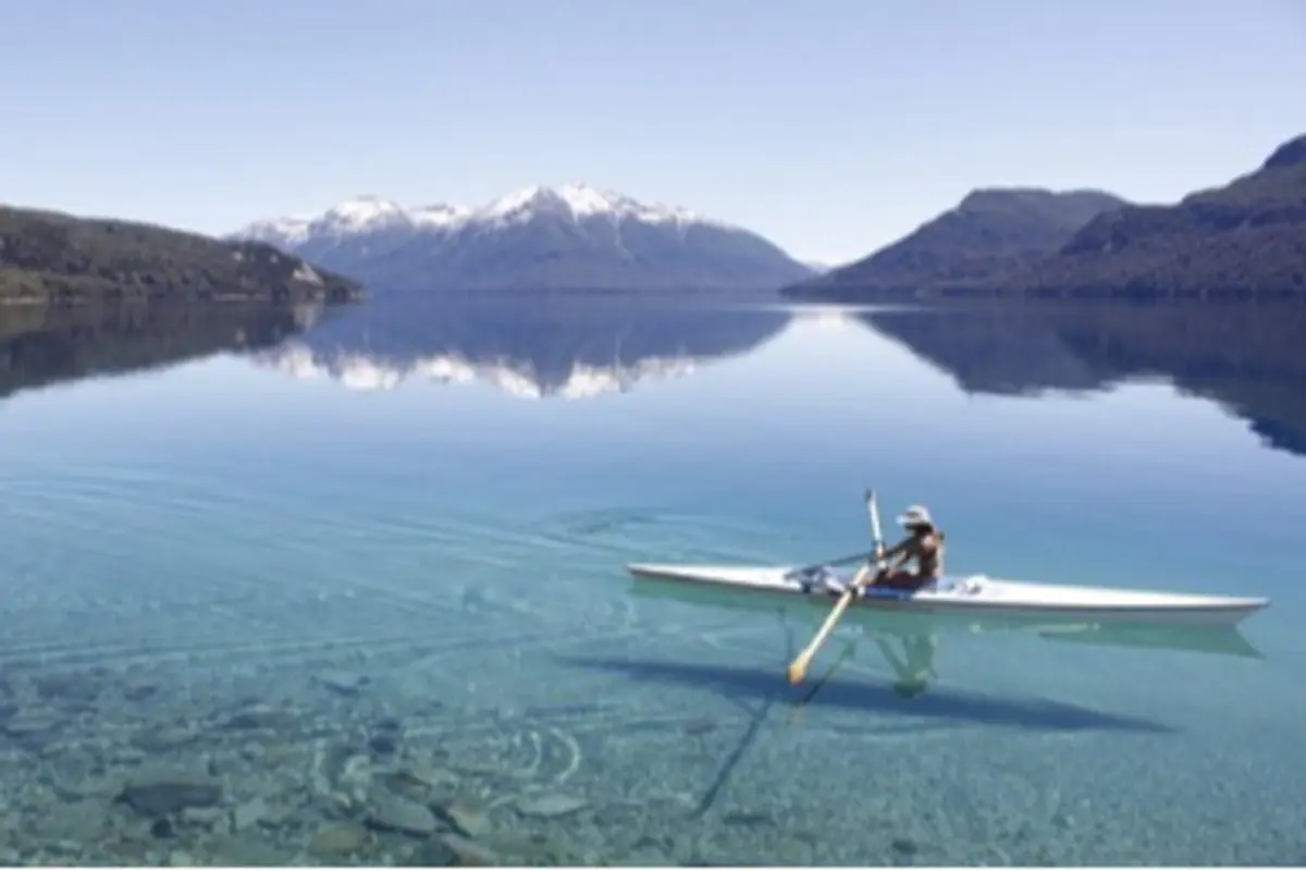 Persona remando en kayak sobre un lago de agua cristalina rodeado de montañas nevadas en un día despejado
