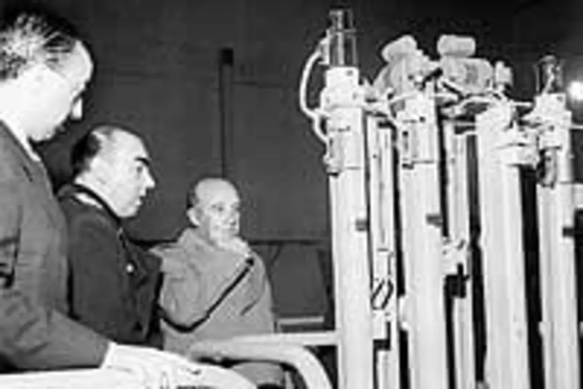 Carrero Blanco observa de cerca una gran máquina industrial en una fábrica antigua en blanco y negro